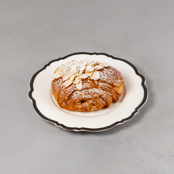 Croissant with powdered sugar and almonds on a decorative plate against a gray background