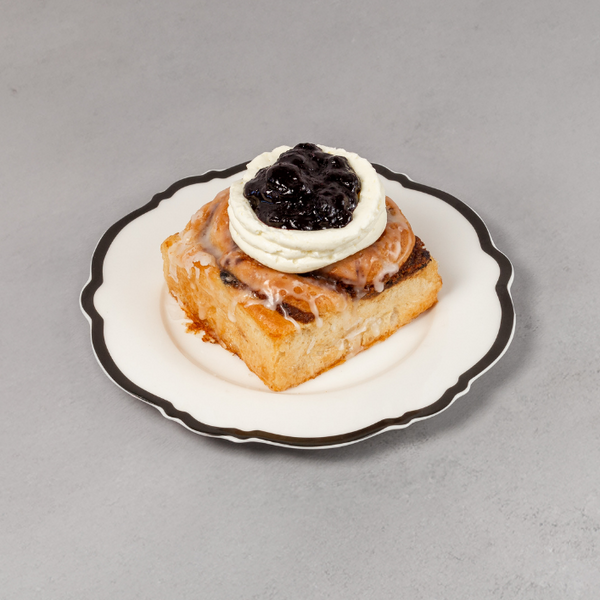 Pastry with cream and black topping on a small plate against a gray background
