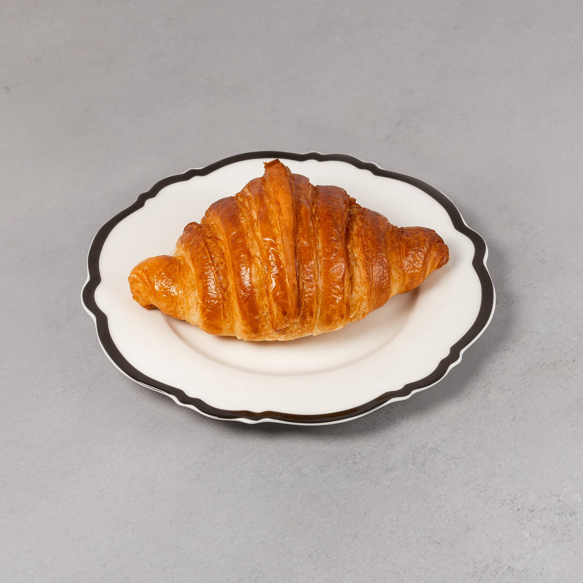 Croissant on a small white plate with black rim on a gray background