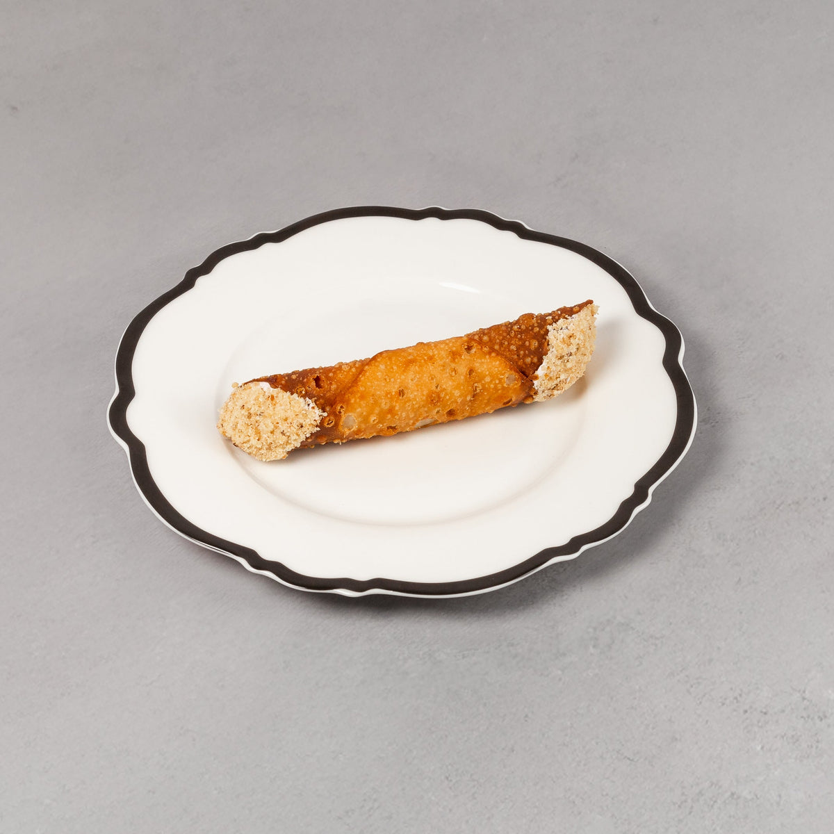 Small rolled-up pastry on a decorative white plate with black rim against a gray background