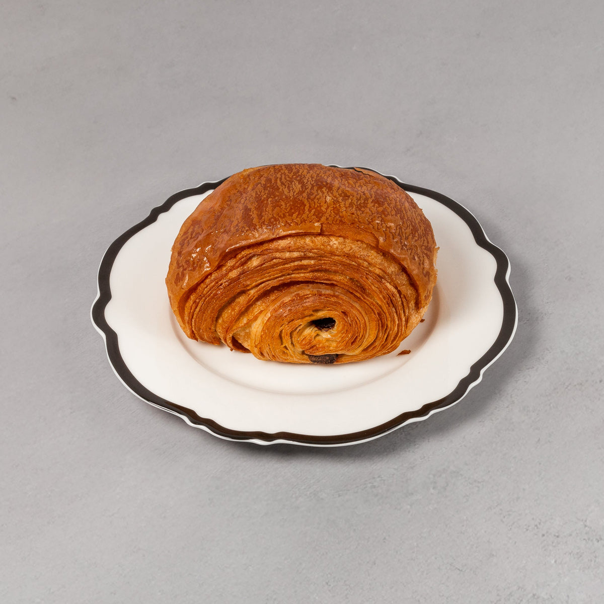 Croissant on a small white plate with black rim on a gray background