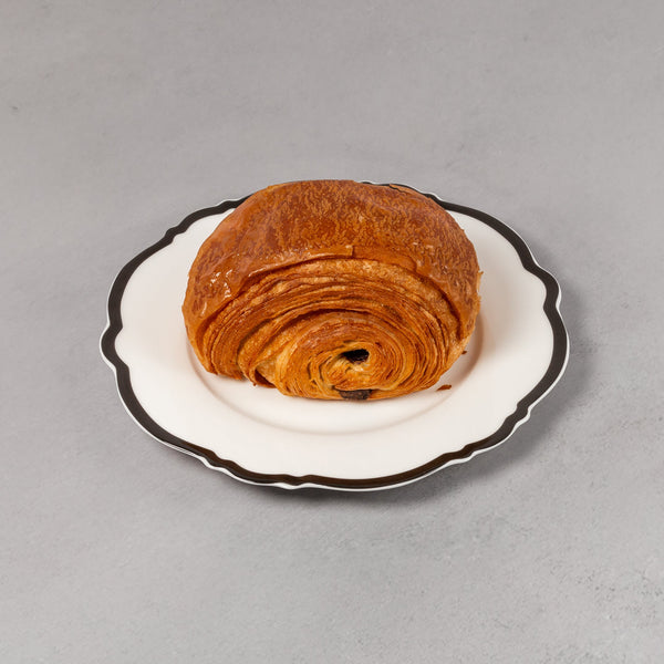Croissant on a small white plate with black rim on a gray background