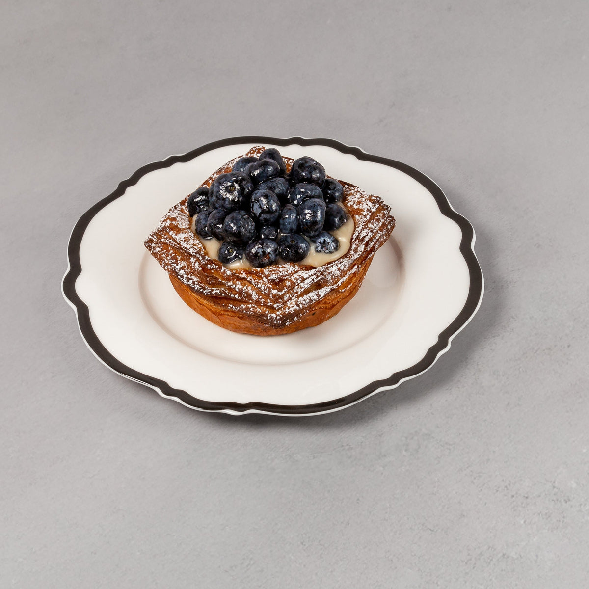 Small pastry with blueberries on a decorative plate against a plain background