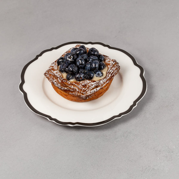 Small pastry with blueberries on a decorative plate against a plain background
