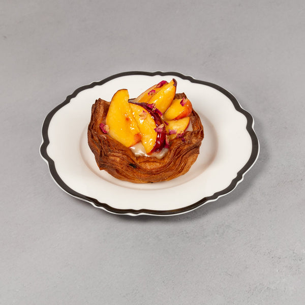 Small pastry with fruit on a white plate with black rim against a gray background