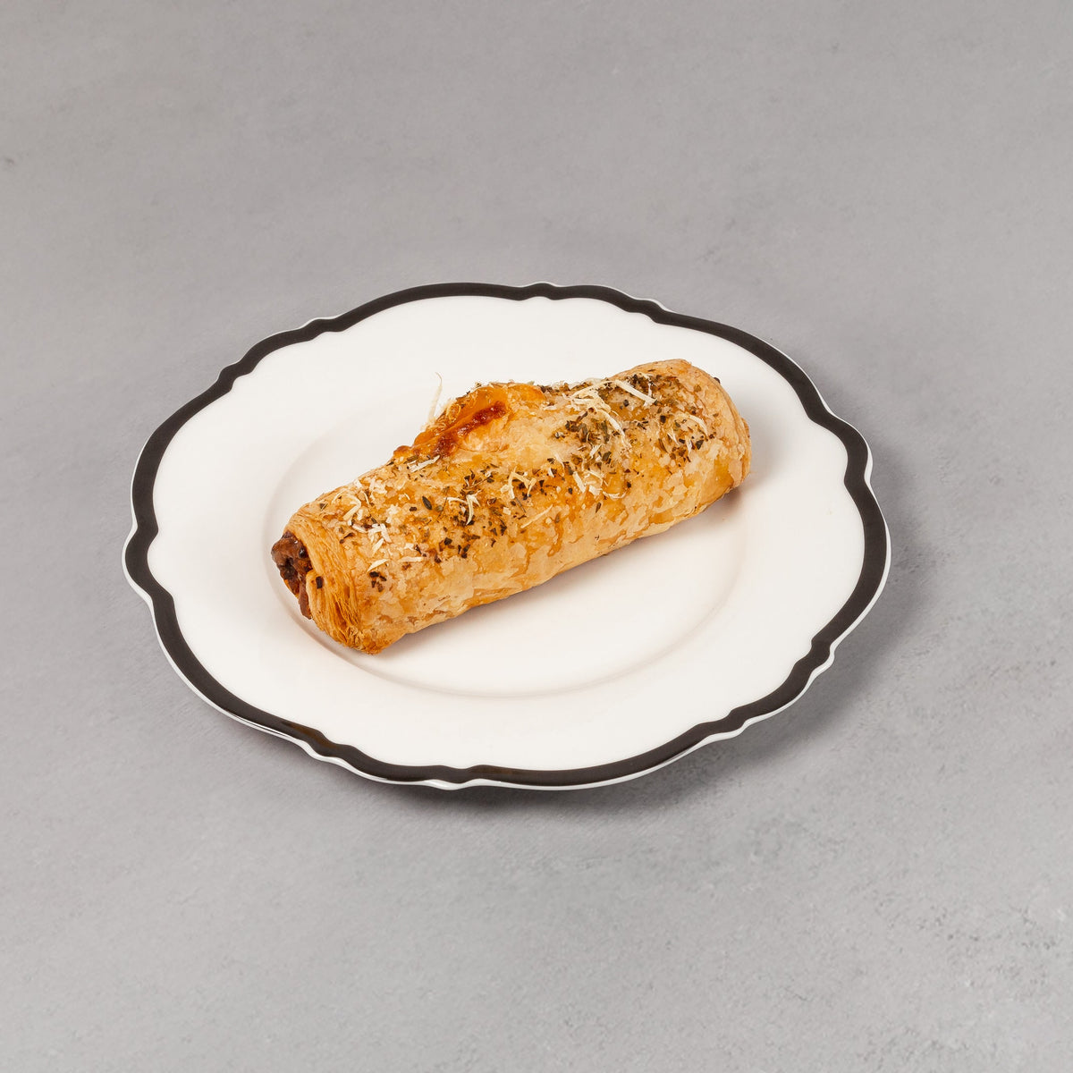 Small rolled pastry on a decorative white plate with black rim on a gray background