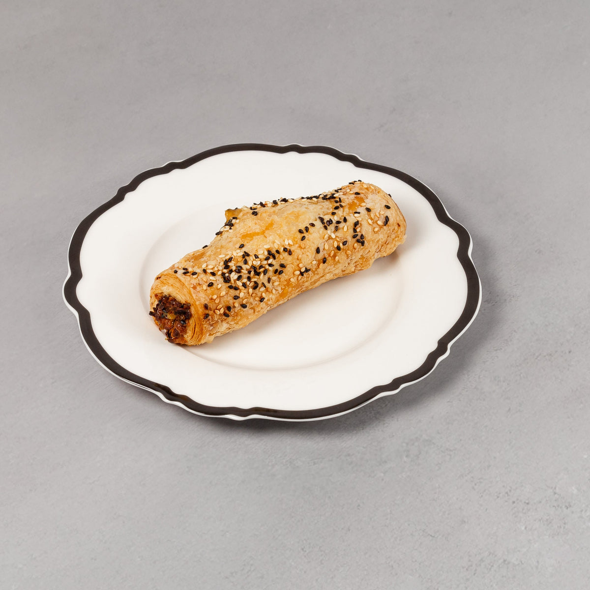 Small pastry on a decorative white plate with black rim on a gray background