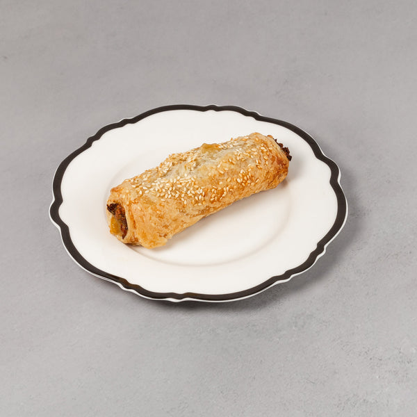 Rolled pastry on a small white plate with black rim on a gray background