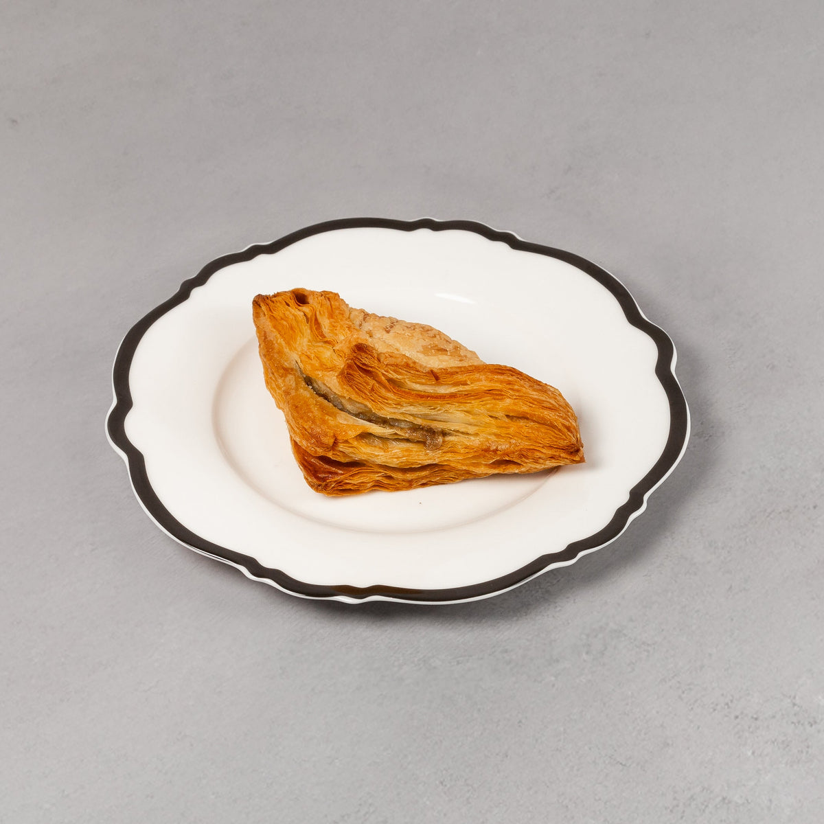 Small piece of food on a white plate with black rim against a gray background